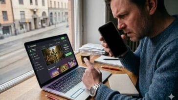 Mies istuu työpöydän ääressä ja tarkastelee vakavana kannettavan tietokoneen näytöllä näkyvää nettikasinosivustoa. Taustalla näkyy ruotsalainen kaupunkimaisema ikkunasta.