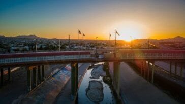 Yhdysvaltain ja Meksikon välinen rajasilta auringonlaskussa — kuvituskuva karteллien toiminnasta raja-alueella